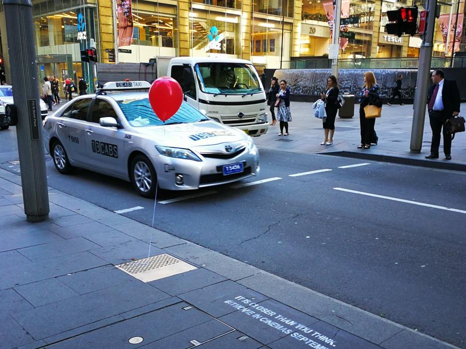 Image of a red helium balloon tied to the lid of a drainage line on a busy street
