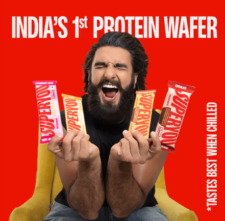 Ranveer Singh holding multiple SuperYou protein wafer bars against a bright red background. 