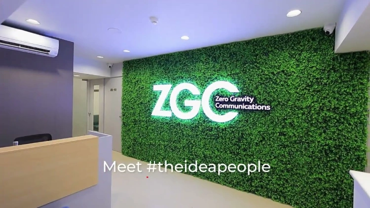 Modern office reception area with a green wall featuring the illuminated “ZGC Zero Gravity Communications” 