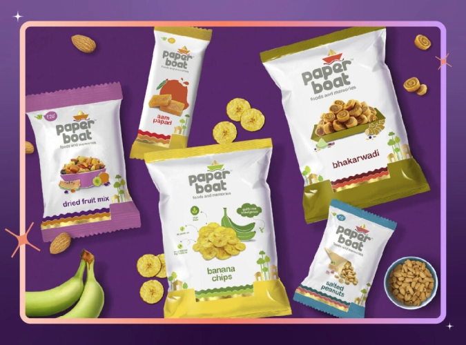 An assortment of Paper Boat packaged snacks including banana chips, bhakarwadi, dried fruit mix, salted peanuts, and aam papad displayed on a deep purple background. 