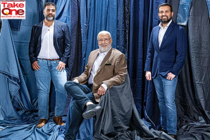 Three Arvind Mills leaders posing against a backdrop of blue denim fabrics