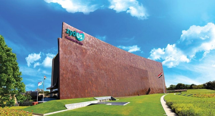 Zydus corporate office building with a large curved brick facade, green lawns, flags